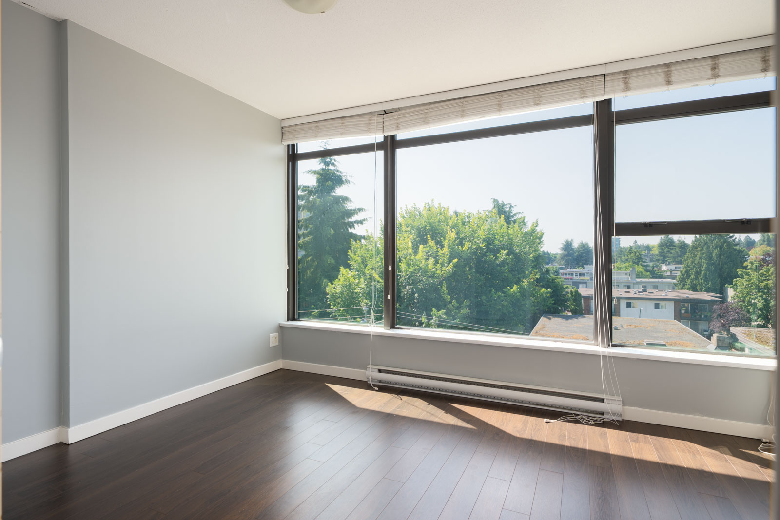 Empty room on 8th floor at 1068 W Broadway, Vancouver, with large windows, white blinds, dark wood floors; city view outside.