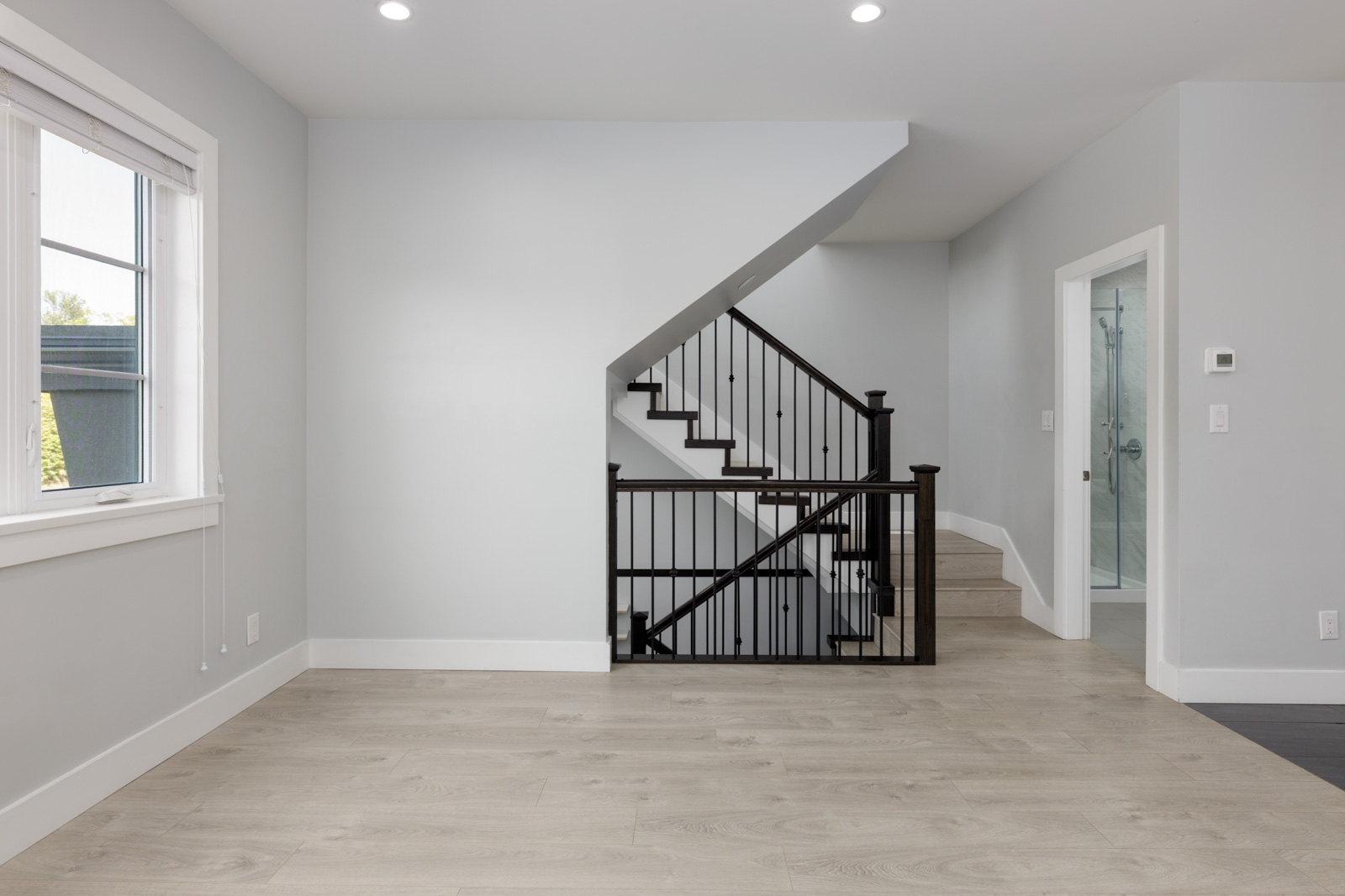 Empty room with light wood floors, gray walls, left-side window, black-railed stairs, and a glass door at 806 Gauthier Ave, Coquitlam.