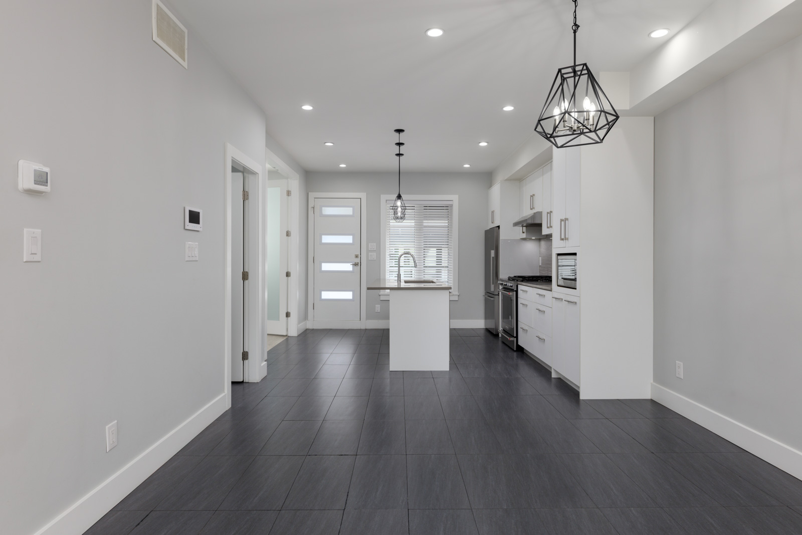 Modern kitchen and dining area in Coquitlam townhouse with gray tile floors, white cabinets, stainless appliances, and pendant lights.