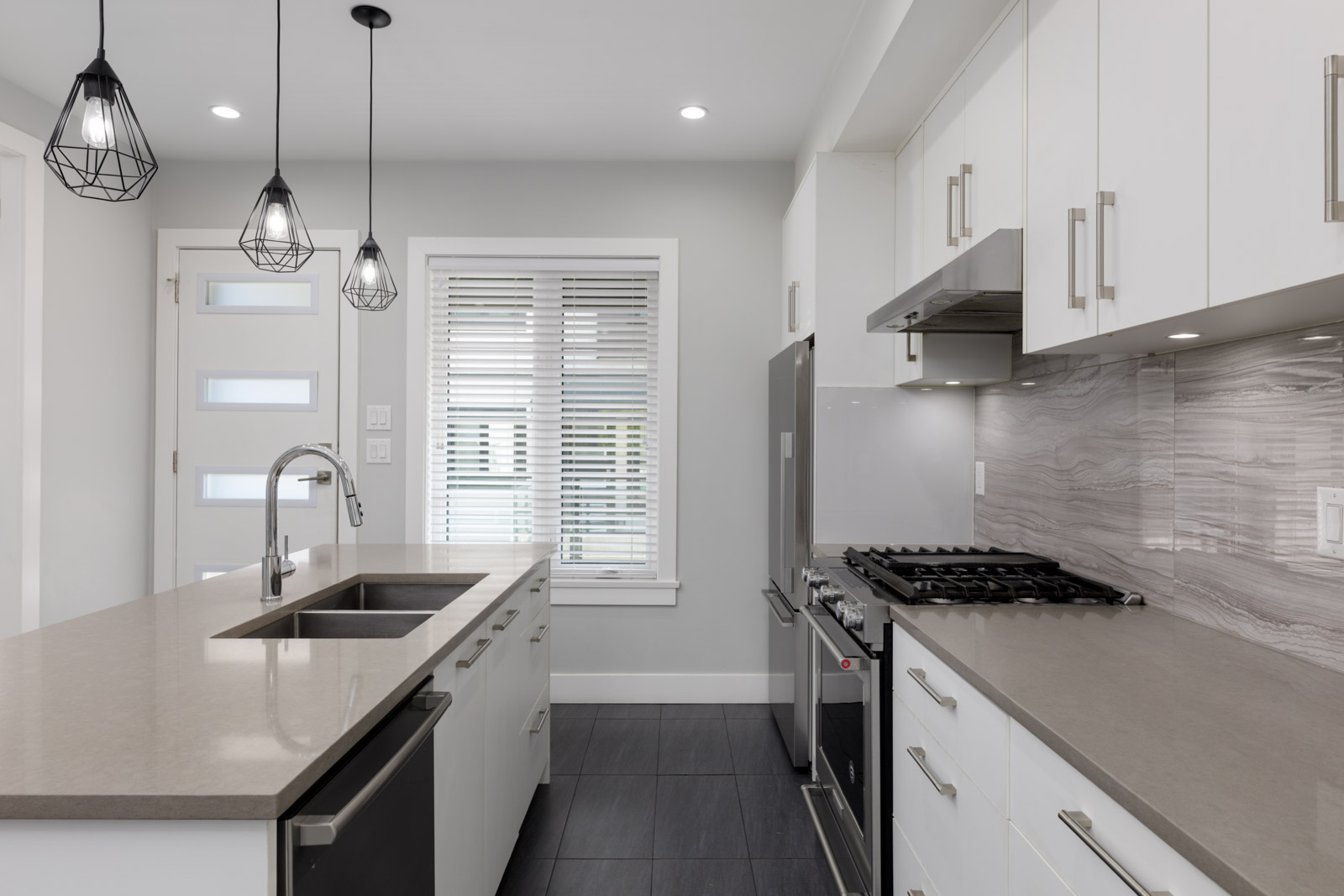 Modern Gauthier Ave townhouse kitchen with white cabinets, gray counters, stainless appliances, island sink, and window blinds in Coquitlam.