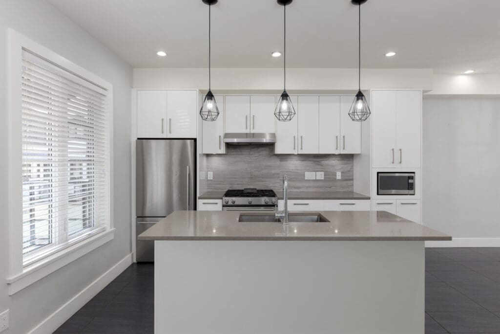 Contemporary kitchen at 806 Gauthier Ave, Coquitlam, with white cabinets, stainless appliances, island sink, and large window blinds.