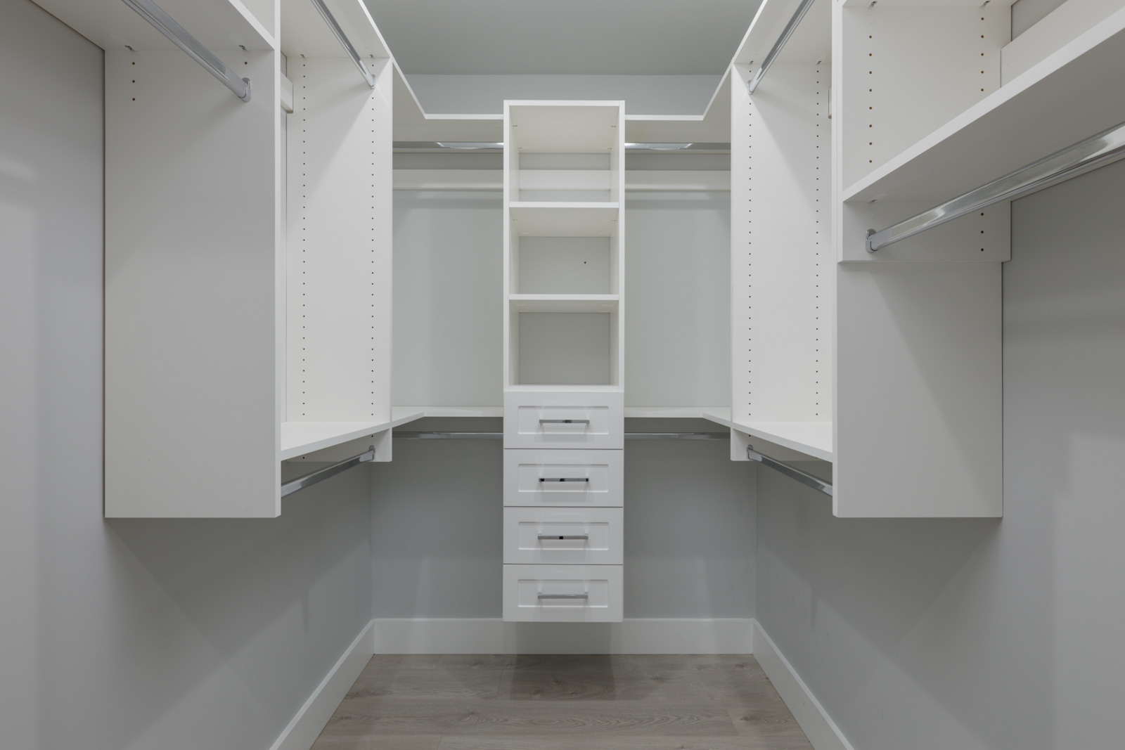 Spacious empty walk-in closet with white shelves and rods, light gray walls, and wood flooring in a townhouse at 806 Gauthier Ave, Coquitlam.