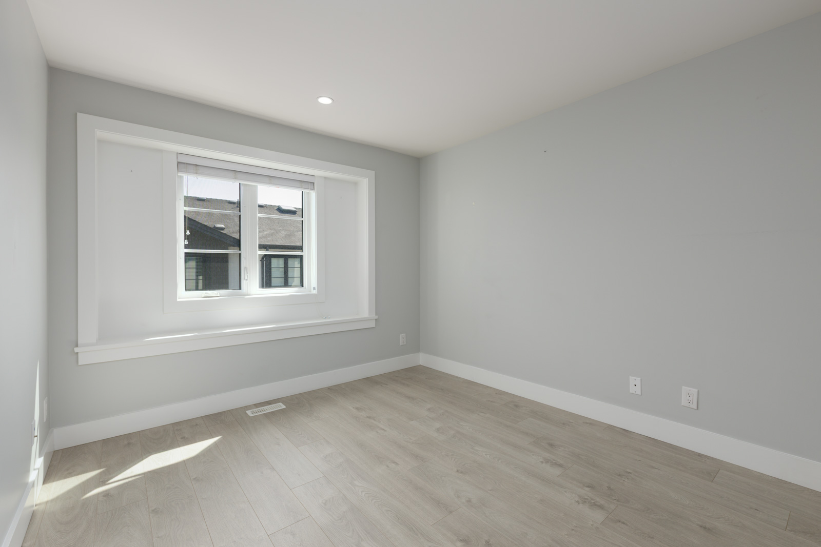 Empty room in a modern Coquitlam townhouse with light gray walls, wood floors, a rectangular window, and recessed ceiling lights.