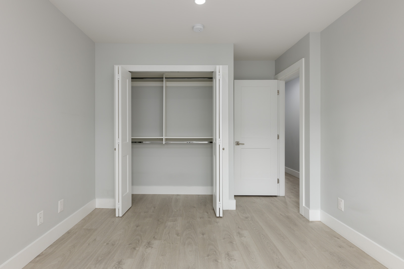 Empty room with light gray walls, wood floors, open closet with white doors, and open door to another area in Coquitlam townhouse.