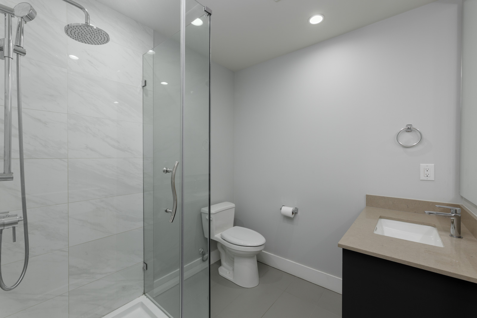 Coquitlam townhouse bathroom with glass shower, toilet, wall-mounted paper holder, rectangular sink, and beige countertop.