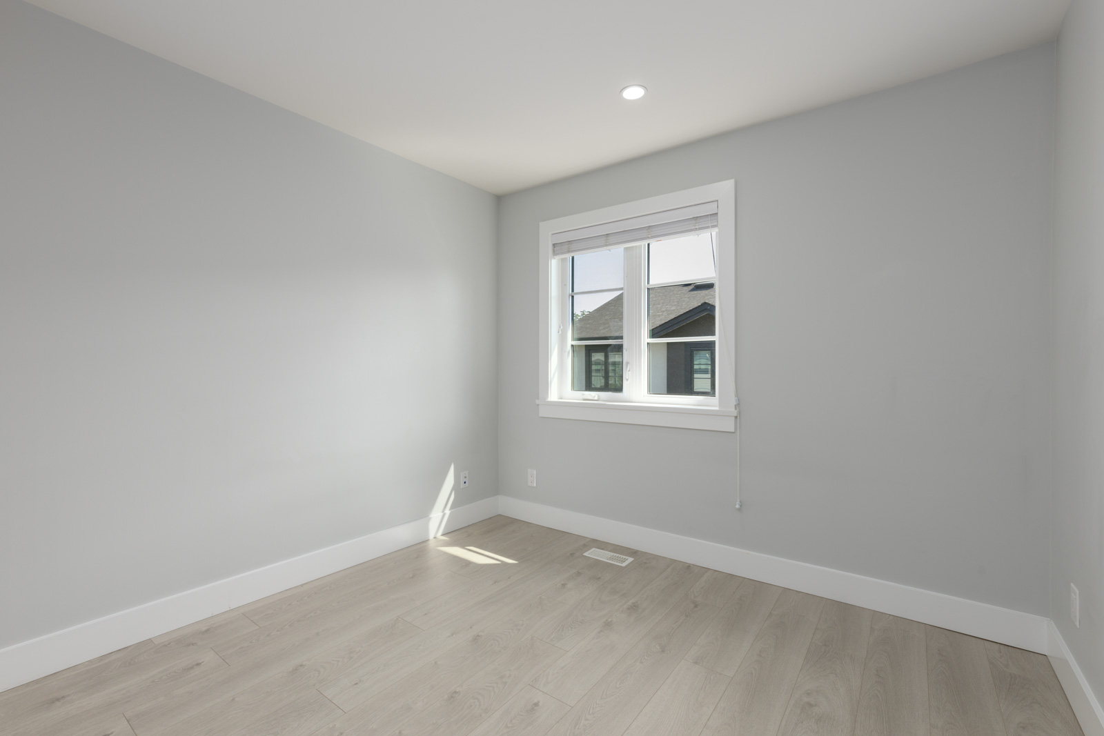 Empty room in a modern Coquitlam townhouse with light gray walls, wood floor, white trim, single window, and ceiling light. 806 Gauthier Ave.