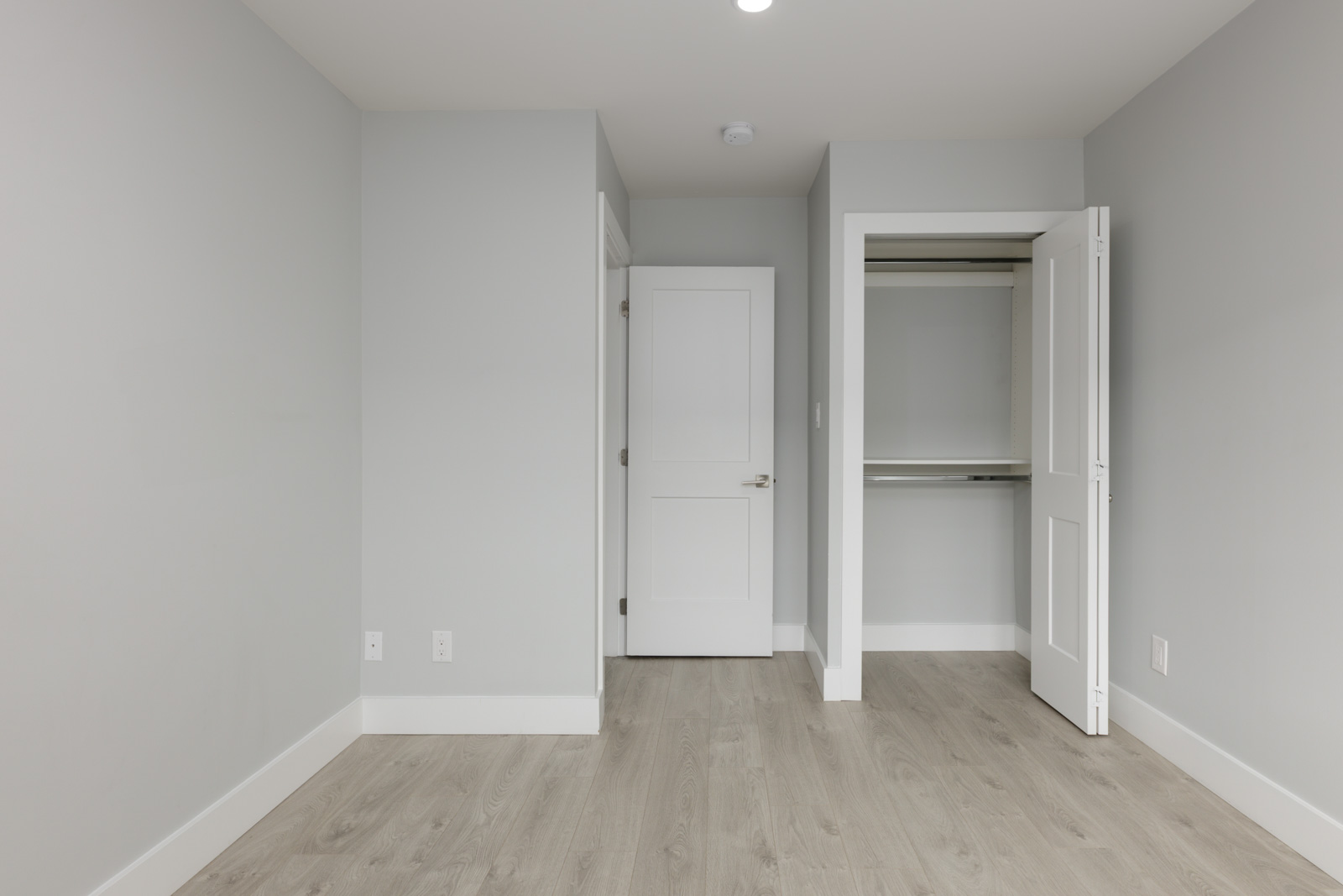 Empty room in a Coquitlam townhouse at 806 Gauthier Ave with light gray walls, wood floors, closet, closed door, and outlets.