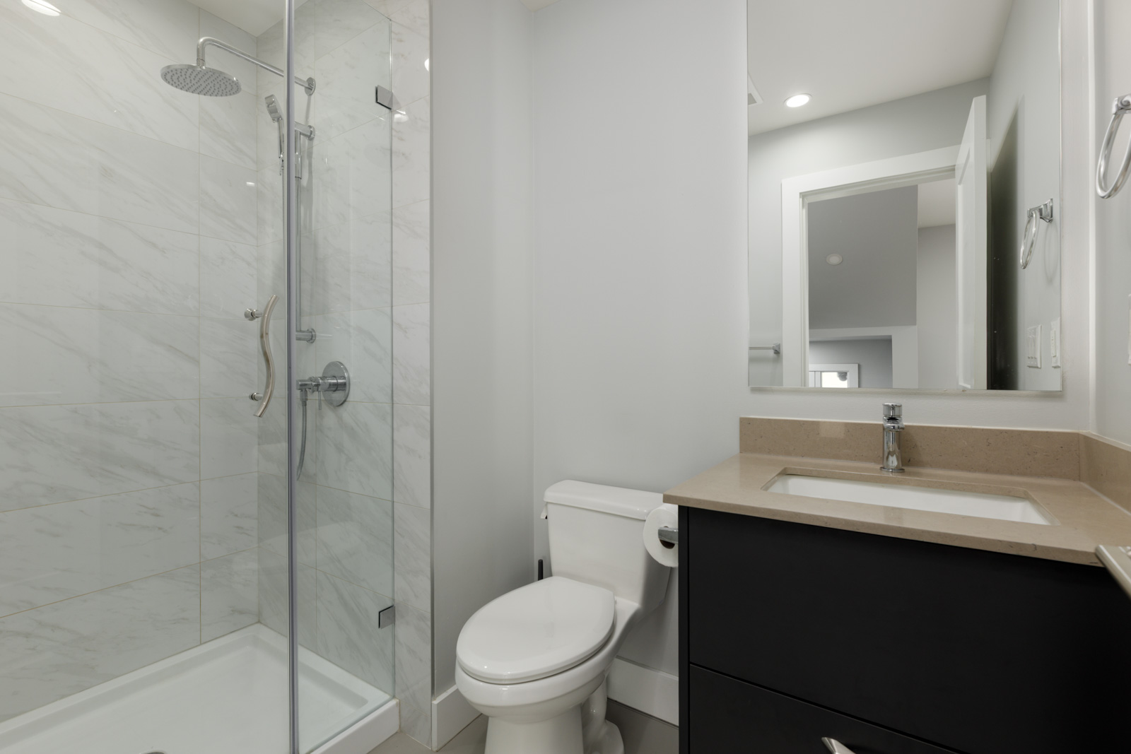 Modern bathroom in Coquitlam townhouse at 806 Gauthier Ave with glass shower, white toilet, black vanity, and wall mirror.