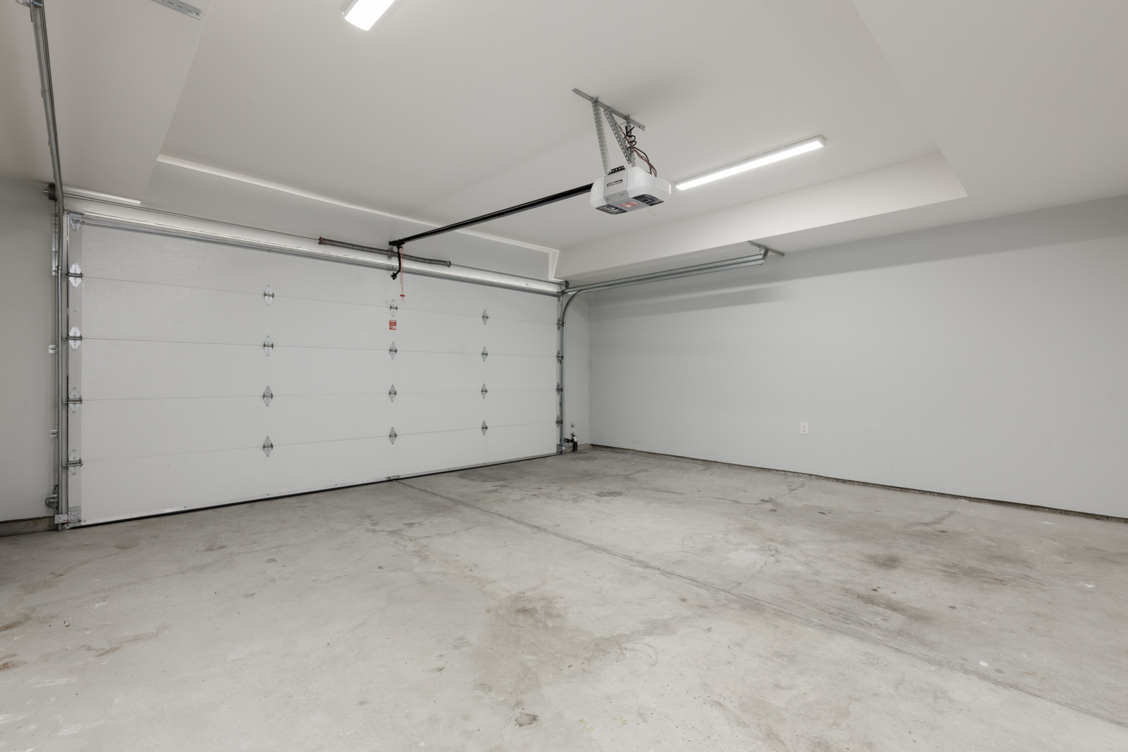 Empty two-car garage in a Coquitlam townhouse with white walls, concrete floor, closed overhead door, lights, and opener.
