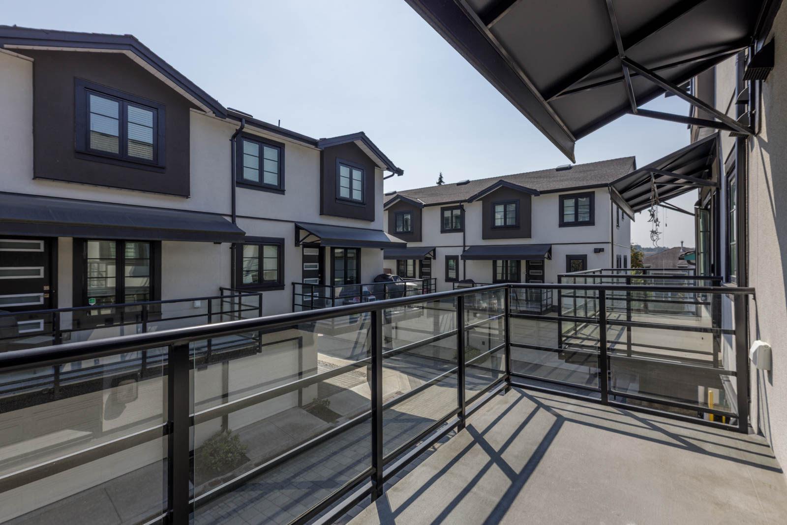 Balcony view of modern townhouses on Gauthier Ave, Coquitlam; black window trim, glass railings, concrete paths, sunny day.