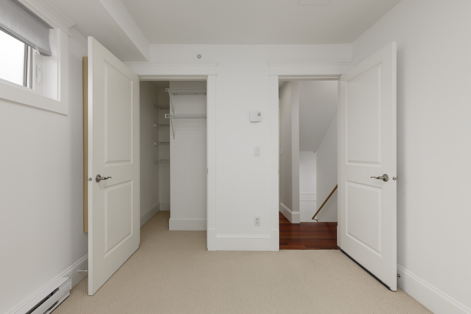Bedroom with beige carpet, white walls, open closet to the left, and a hallway door showing wooden stairs near St Catherines St, Vancouver.