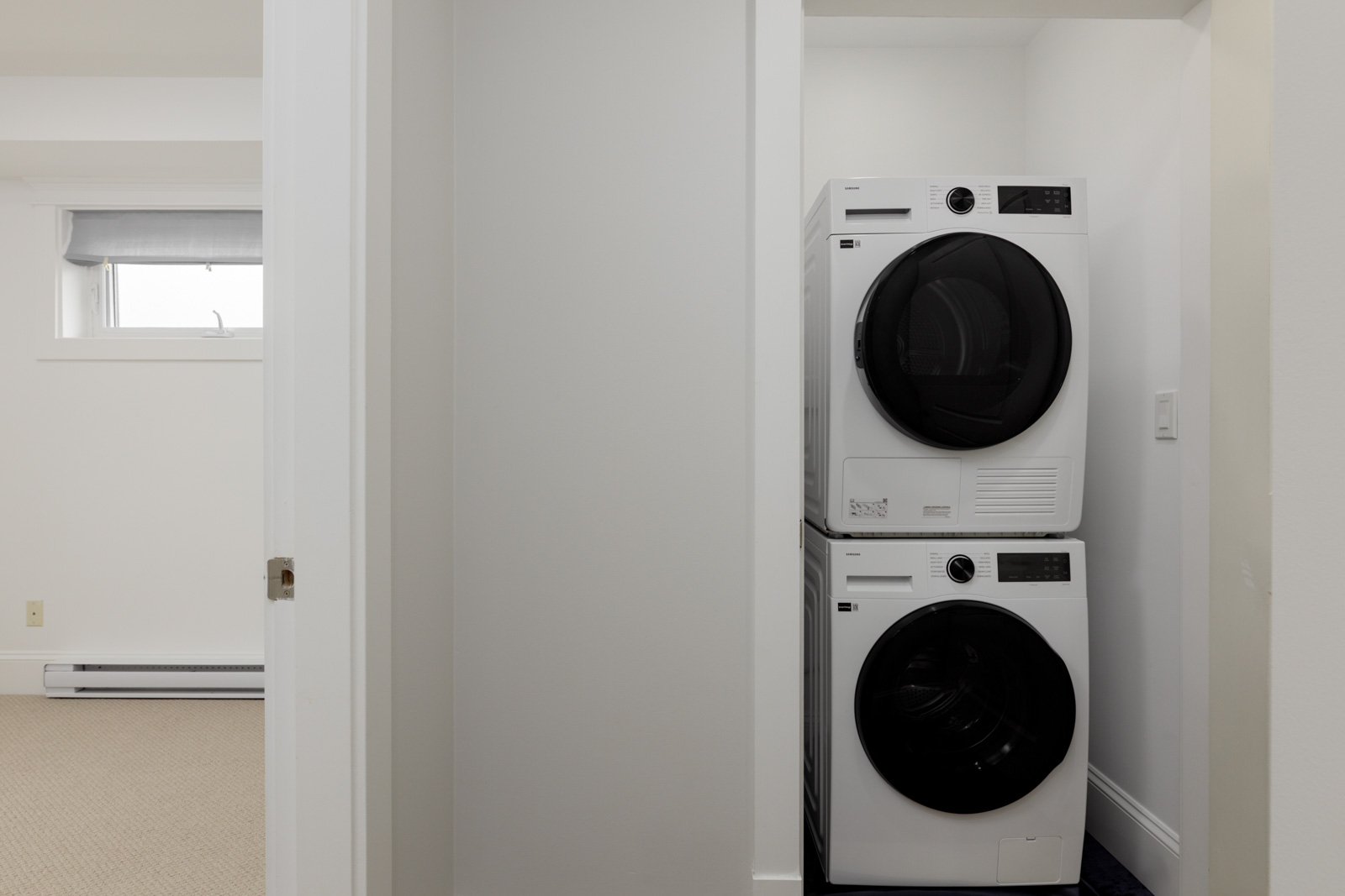 A stacked washer and dryer in a compact laundry nook with white walls and minimal decor near St Catherines St, Vancouver.
