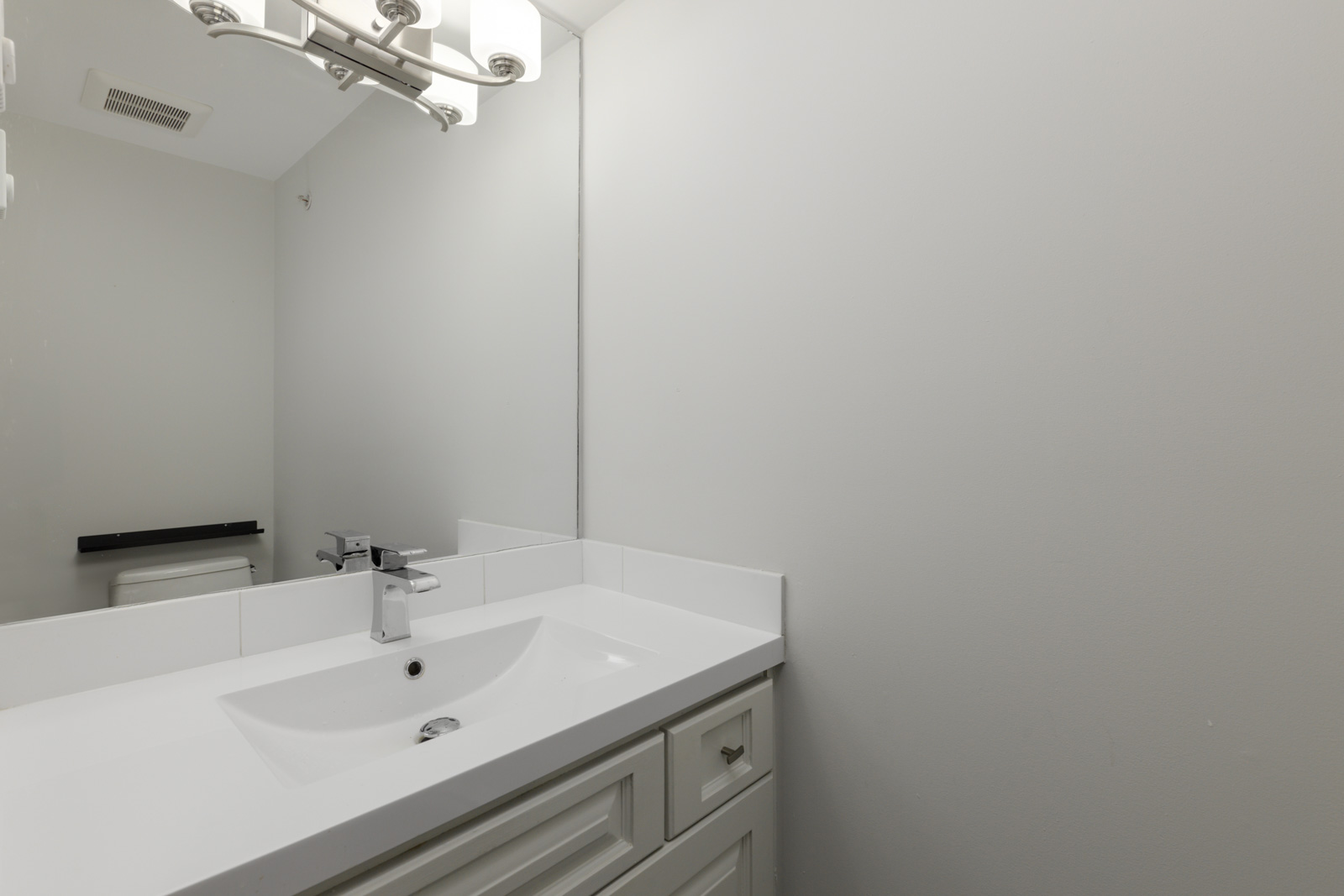 White bathroom with modern vanity, rectangular sink, chrome faucet, mirror, overhead light, and toilet; Vancouver location.
