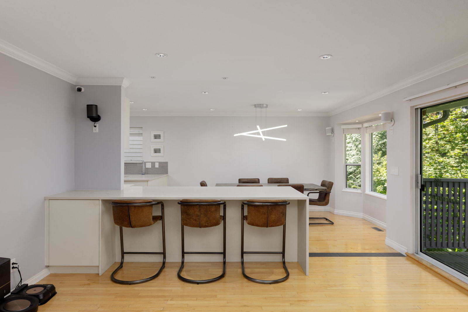 Open kitchen and dining area in Vancouver townhouse, with light wood floors, white walls, breakfast bar, large windows, and balcony door.