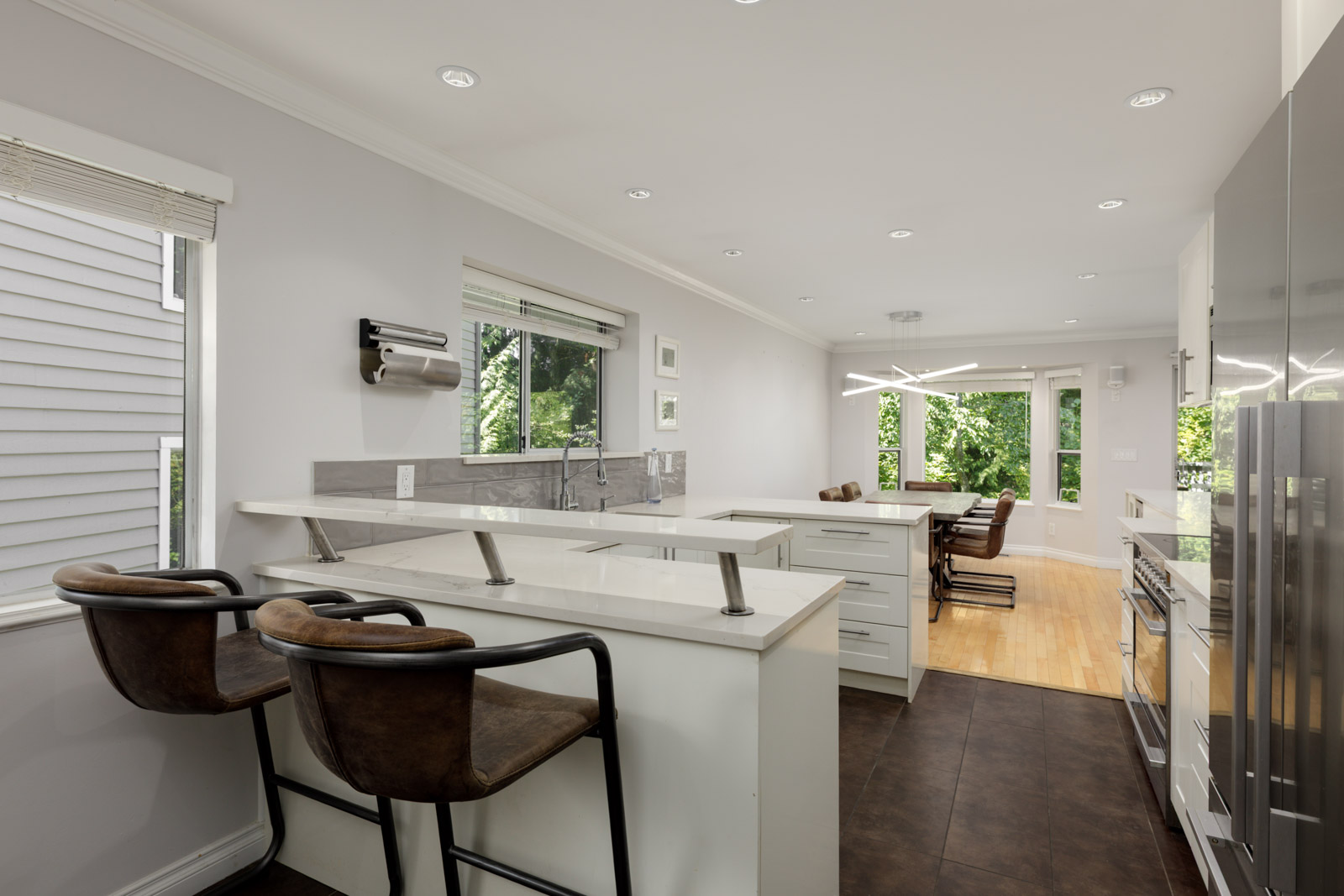 Kitchen at 3634 Garibaldi Dr, Vancouver with white cabinets, stainless steel appliances, large island, and windows facing trees.