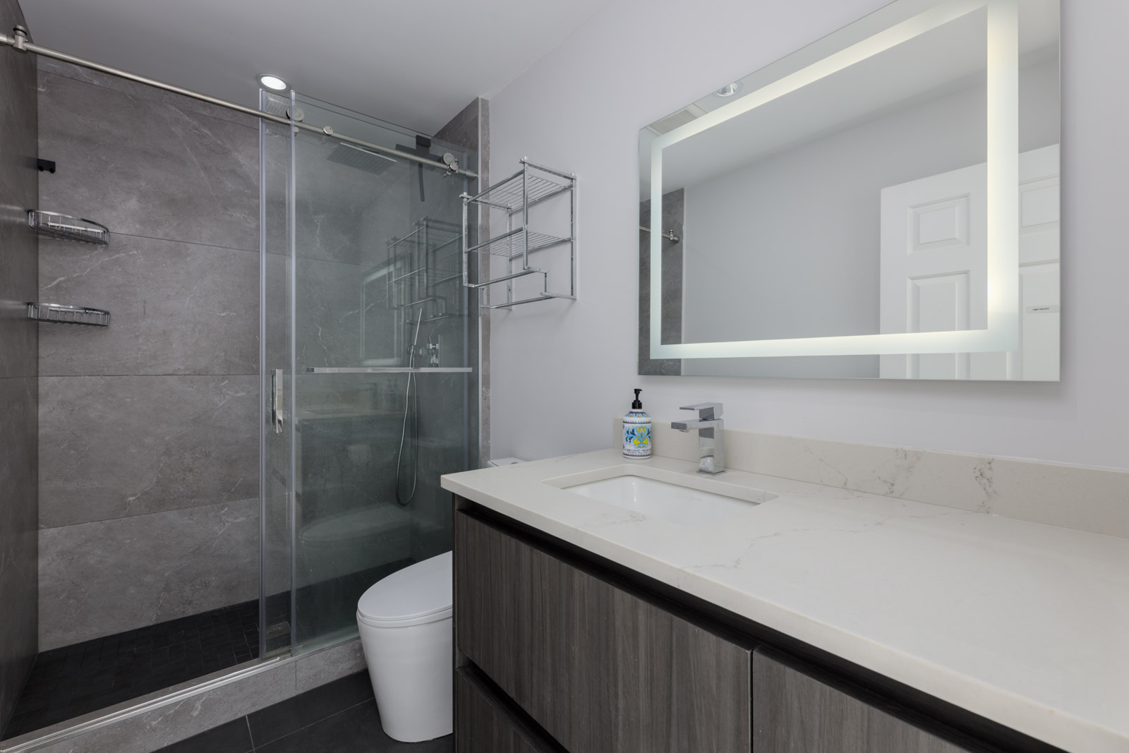 Contemporary bathroom on Garibaldi Dr, Vancouver with glass shower, wall shelves, lit mirror, and marble sink countertop.