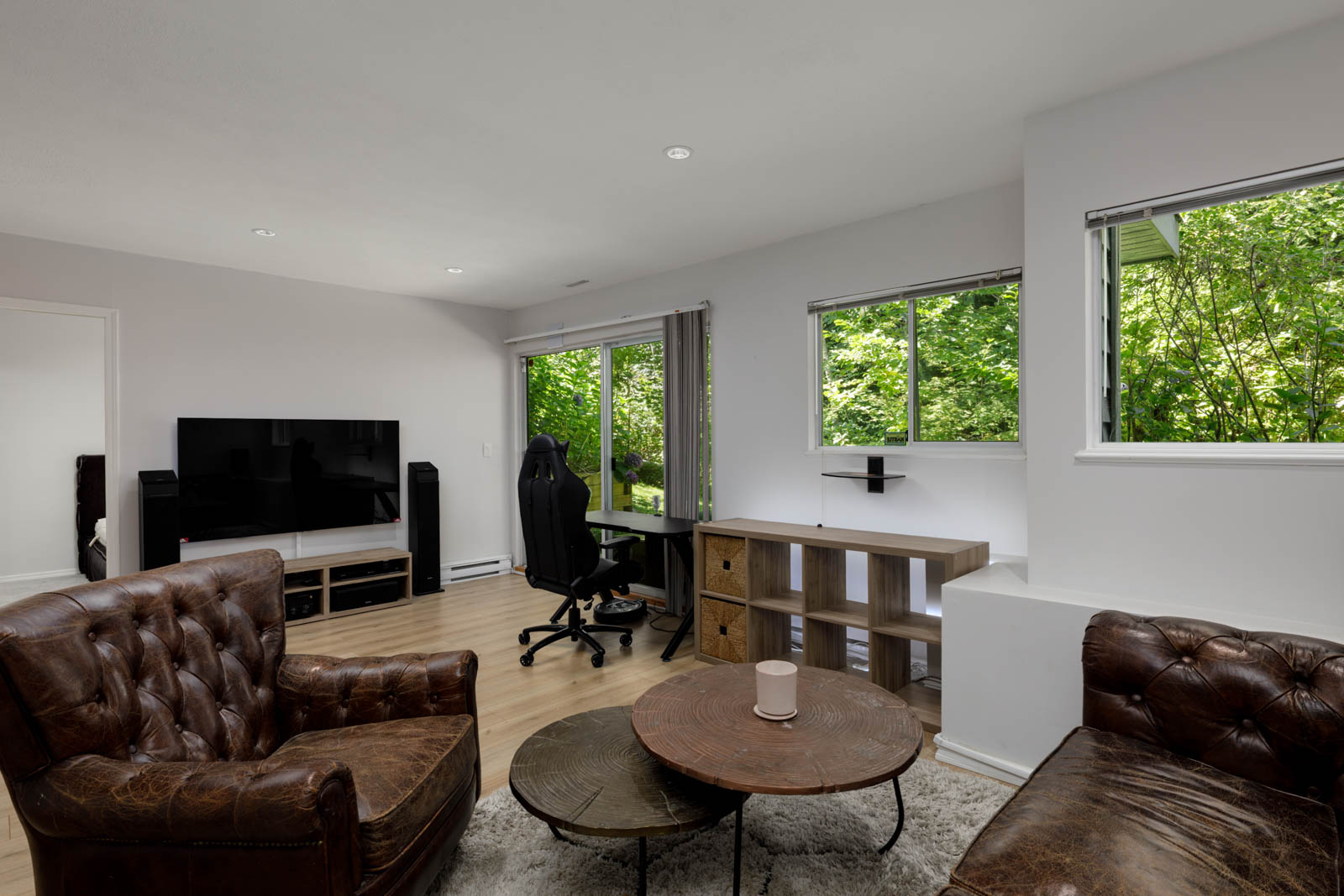 Modern living room in Vancouver townhouse with two leather chairs, round coffee table, TV, desk, and large windows facing trees.
