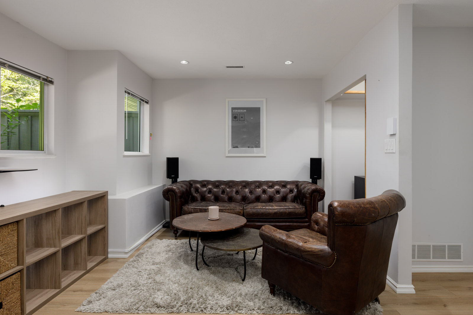 Living room in a Vancouver townhouse with brown leather sofa and chair, round coffee table, beige rug, wood shelves, and garden views.