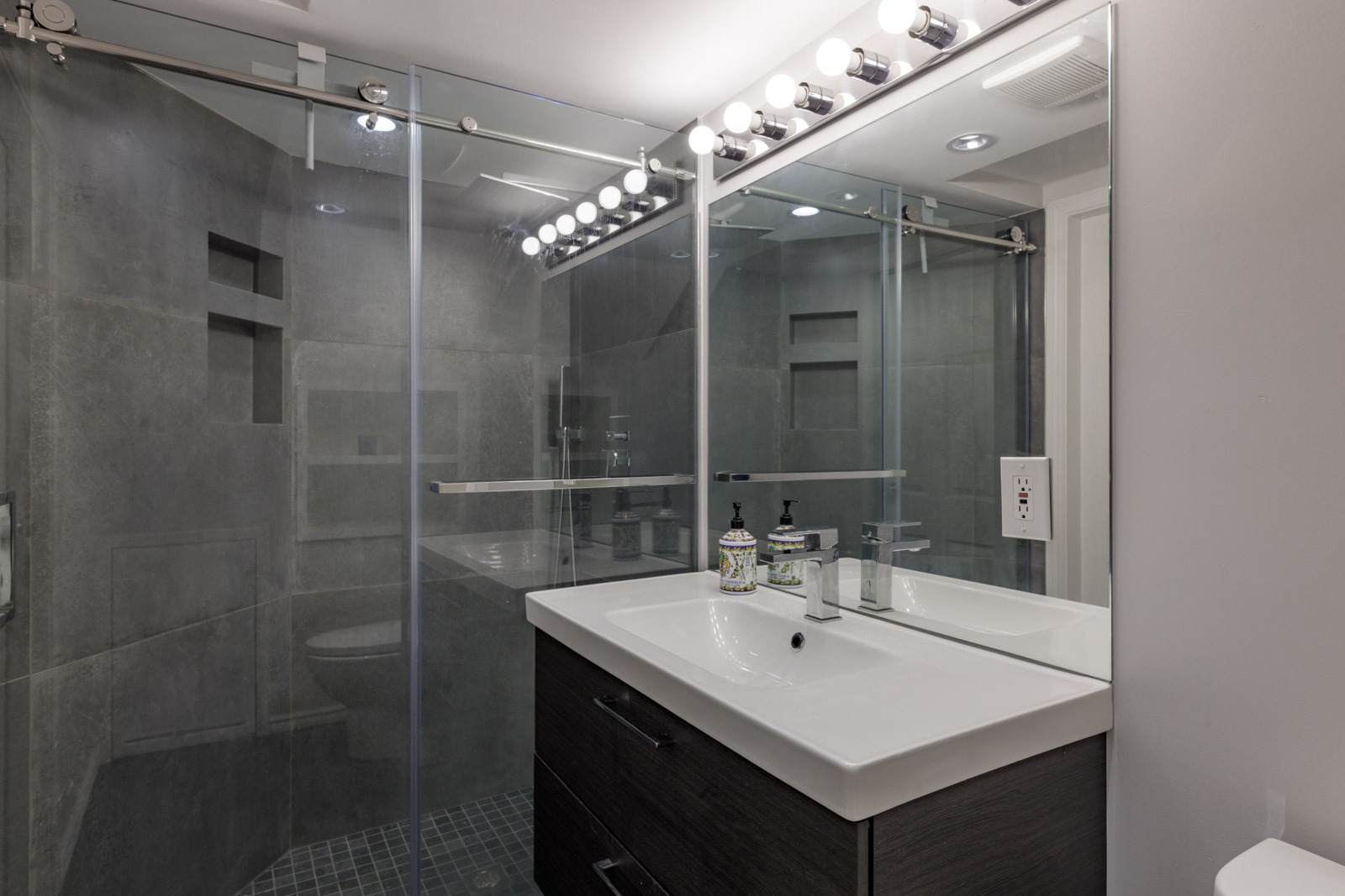 Modern bathroom in a Vancouver townhouse on Garibaldi Dr with glass shower, large mirror, vanity sink, and bright bulb lights.