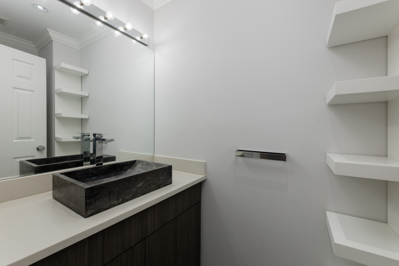Modern bathroom at 3634 Garibaldi Dr, Vancouver with black stone sink, large mirror, white counter, shelves, chrome towel holder.