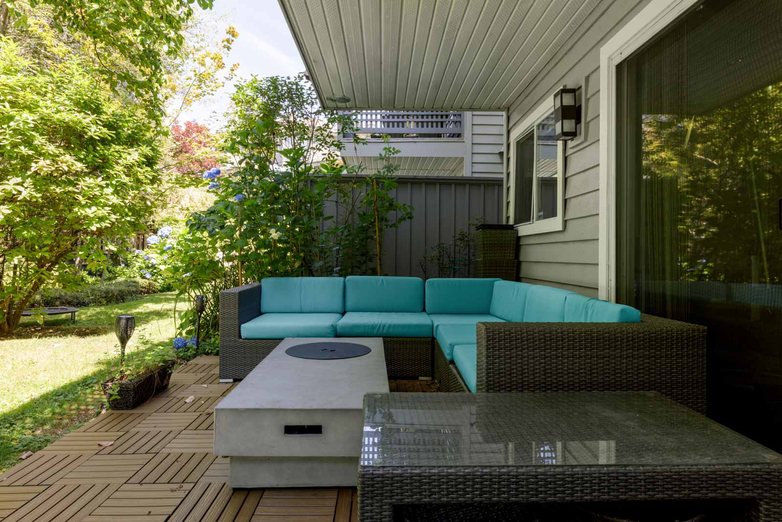 Outdoor patio at 3634 Garibaldi Dr, Vancouver, with wicker seating, turquoise cushions, fire pit table, and leafy garden.