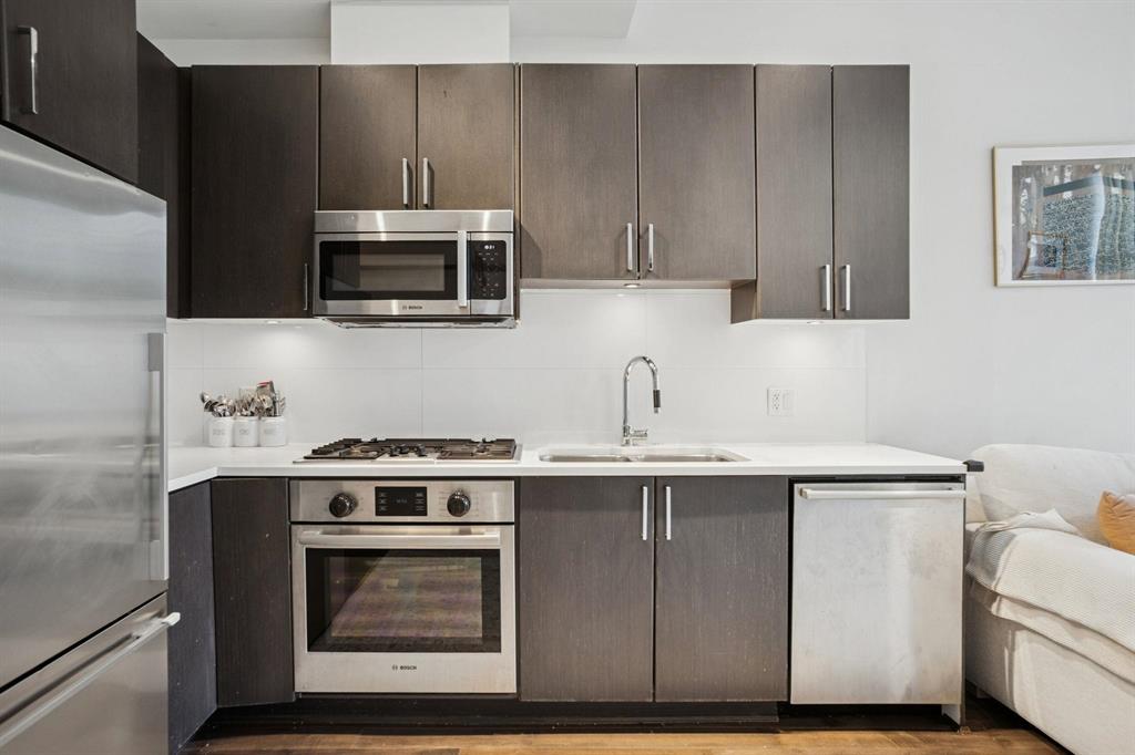 Modern kitchen with dark cabinets, stainless steel appliances, built-in oven, gas stove, and dishwasher by a white sofa.