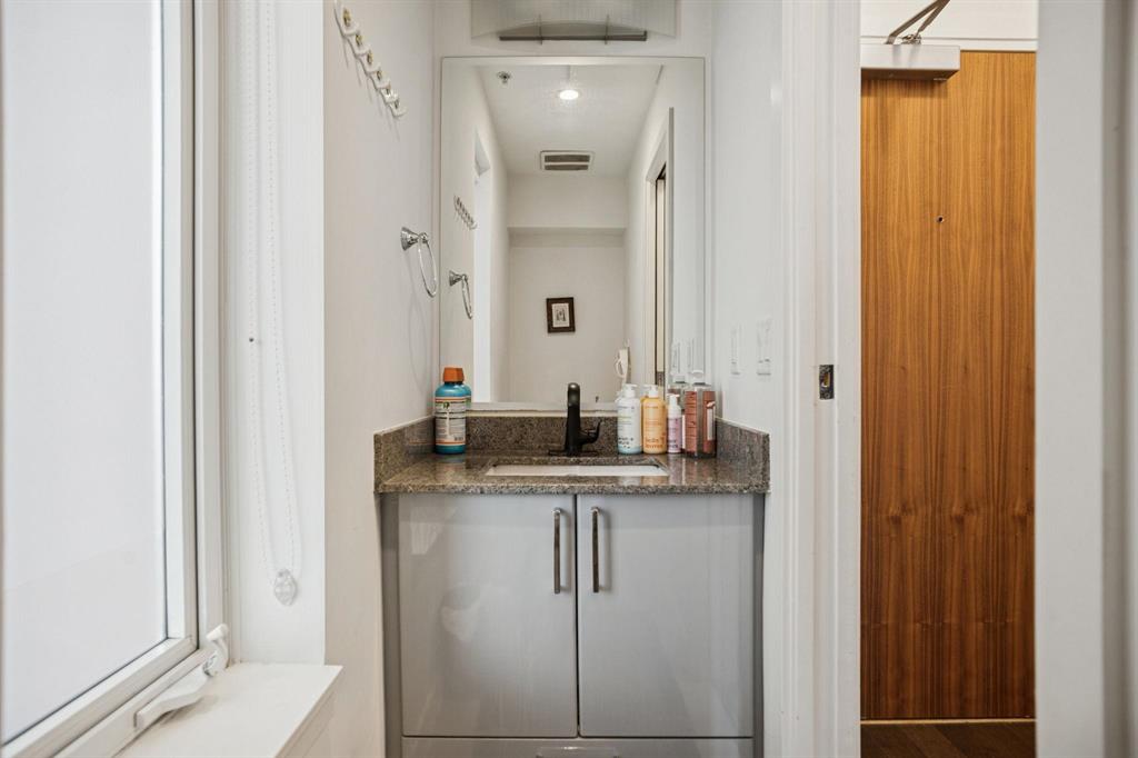 Compact bathroom vanity with granite top, sink, mirror, and toiletries against a white wall near a wooden sliding door.