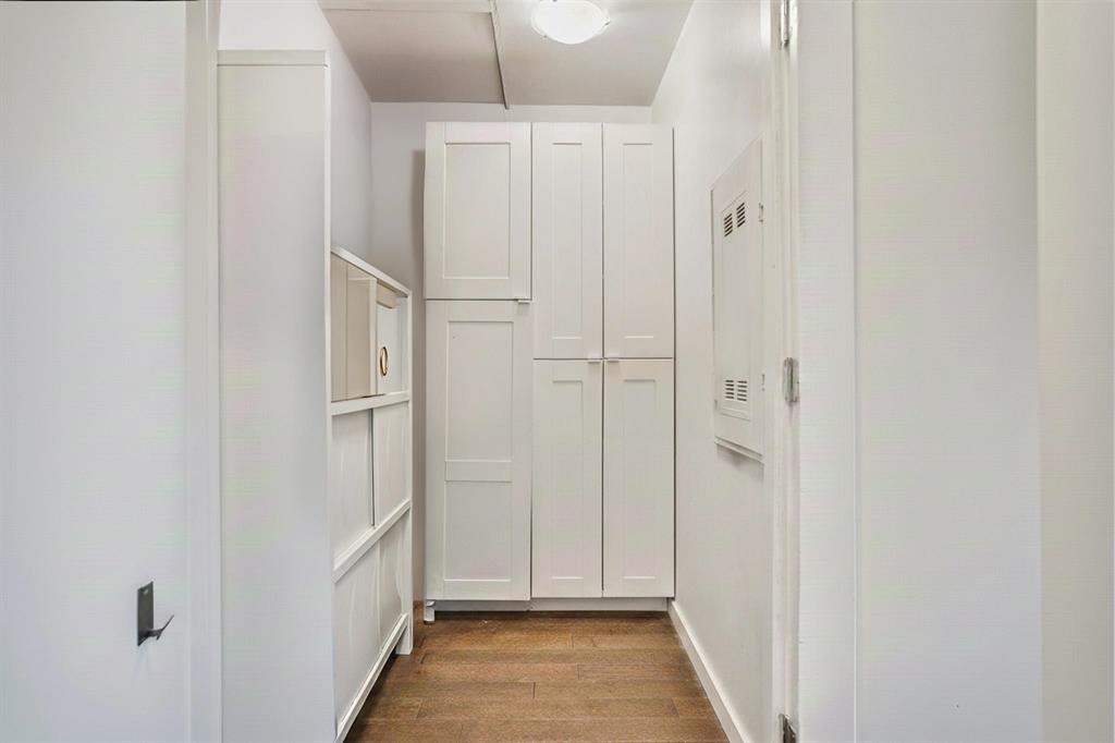Narrow hallway featuring a wooden floor, white cabinets, overhead lighting, and a utility panel mounted on the right wall.