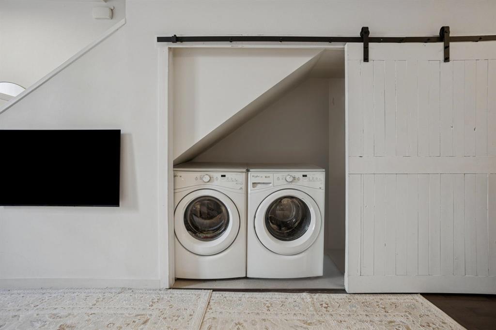 Front-loading washer and dryer side by side in a nook under stairs, partially hidden by a sliding white barn door.