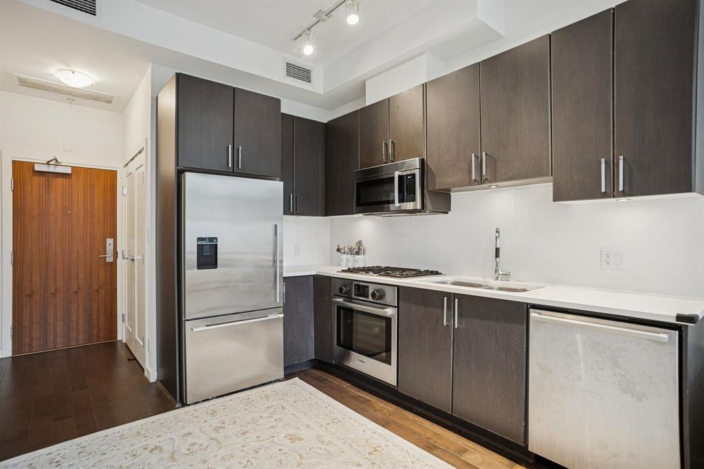 Modern kitchen with dark wood cabinets, stainless steel appliances, white counters, light rug on dark wood floor, and white walls.