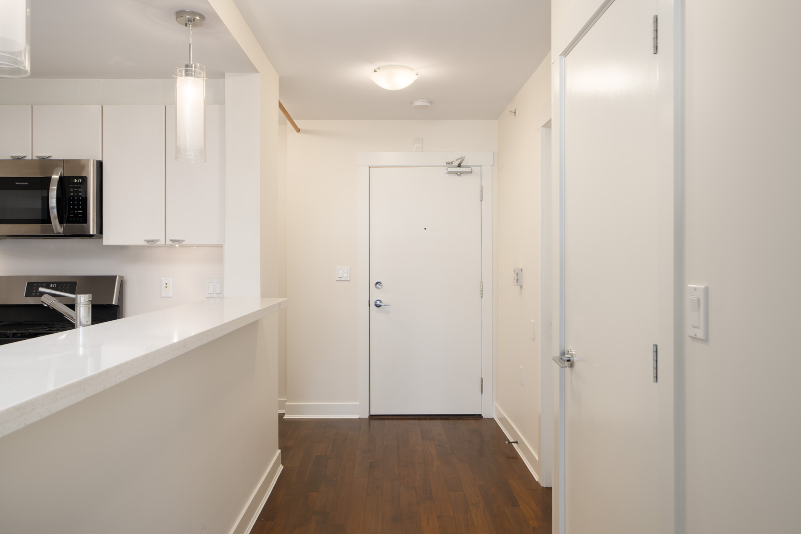 Entryway of a modern 5th floor apartment on 3rd St W, North Vancouver, with white walls, wood floor, open kitchen and stainless appliances.