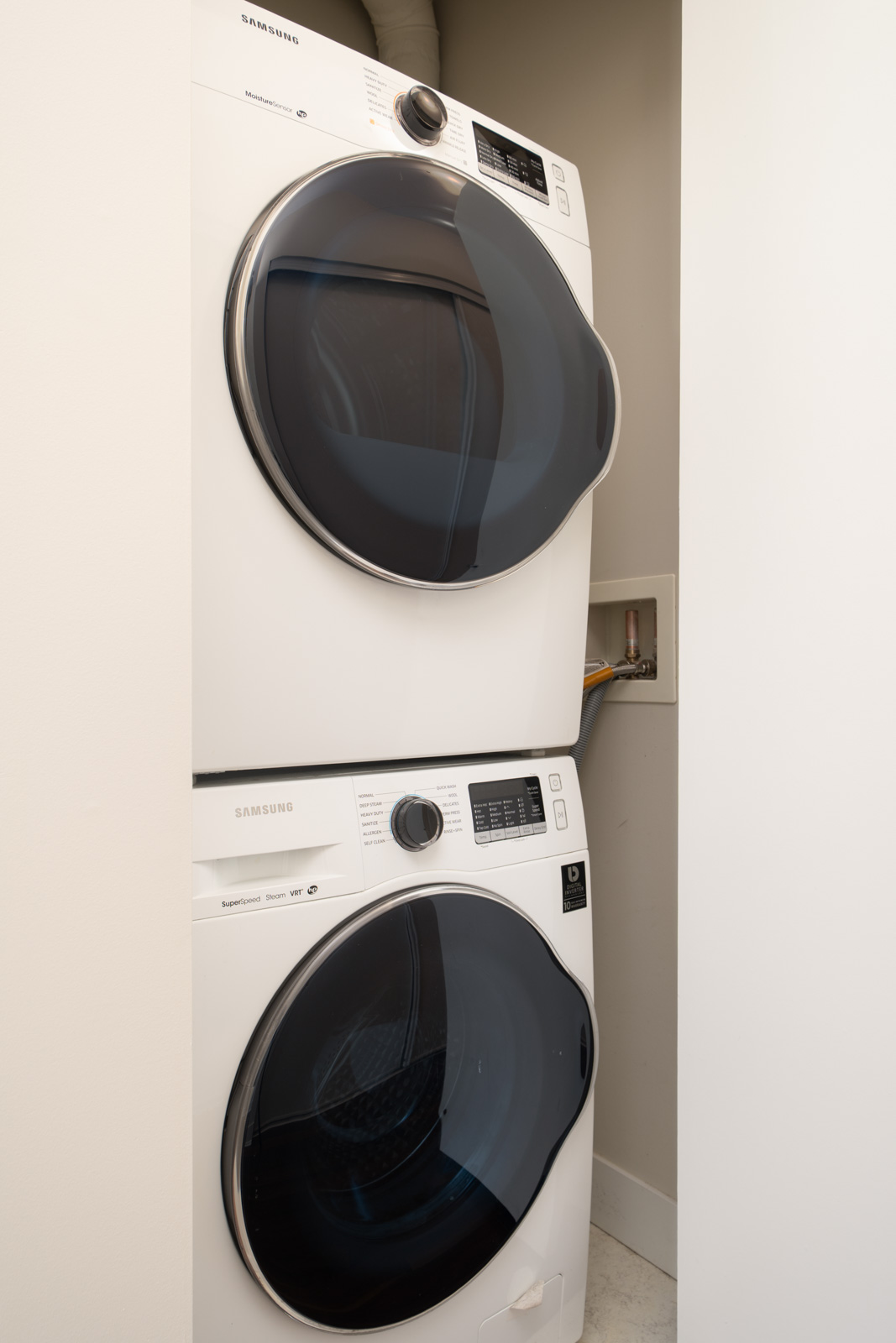 Stacked Samsung washer and dryer in a compact laundry closet with white walls and tiled floor on 5th Floor, 3rd St W, North Vancouver.