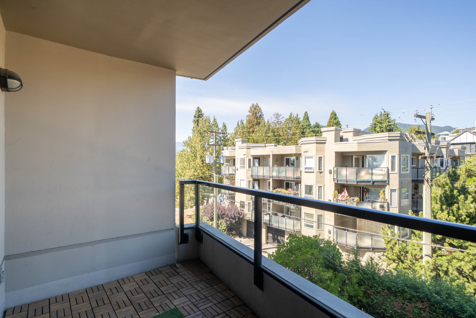View from a 5th floor balcony at 160 3rd St W, North Vancouver, showing apartments, trees, and power lines under clear skies.