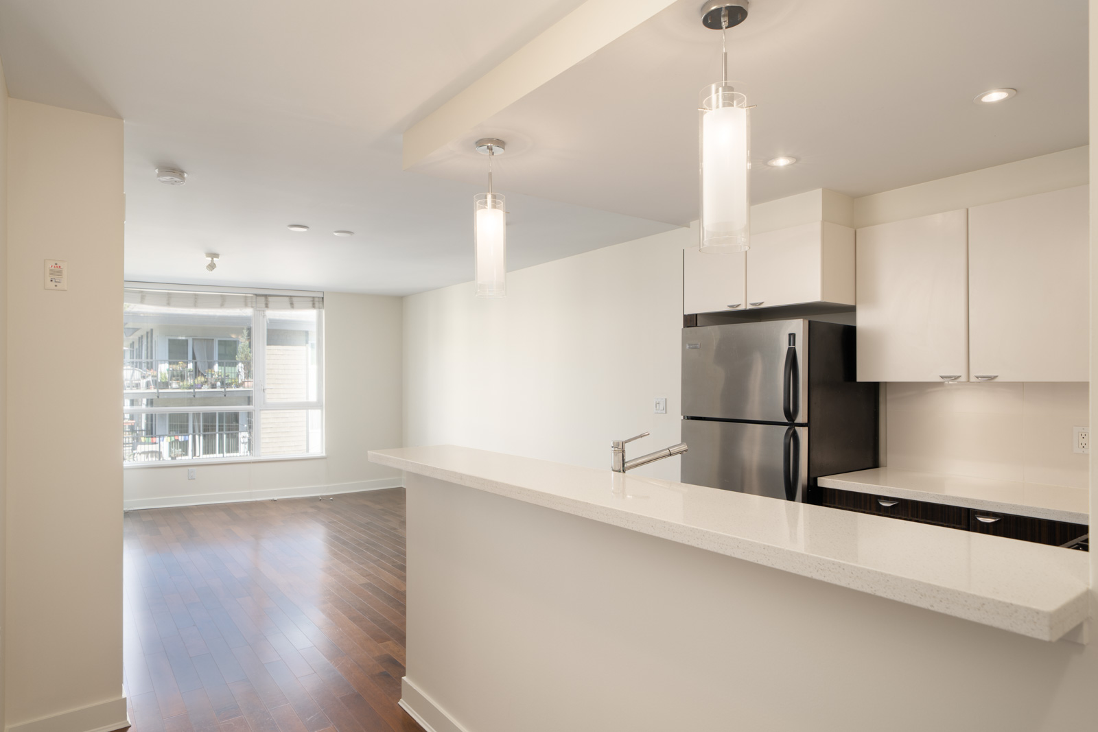 Modern kitchen with white cabinets, stainless steel appliances, long countertop, opens to bright living area with window in North Vancouver.