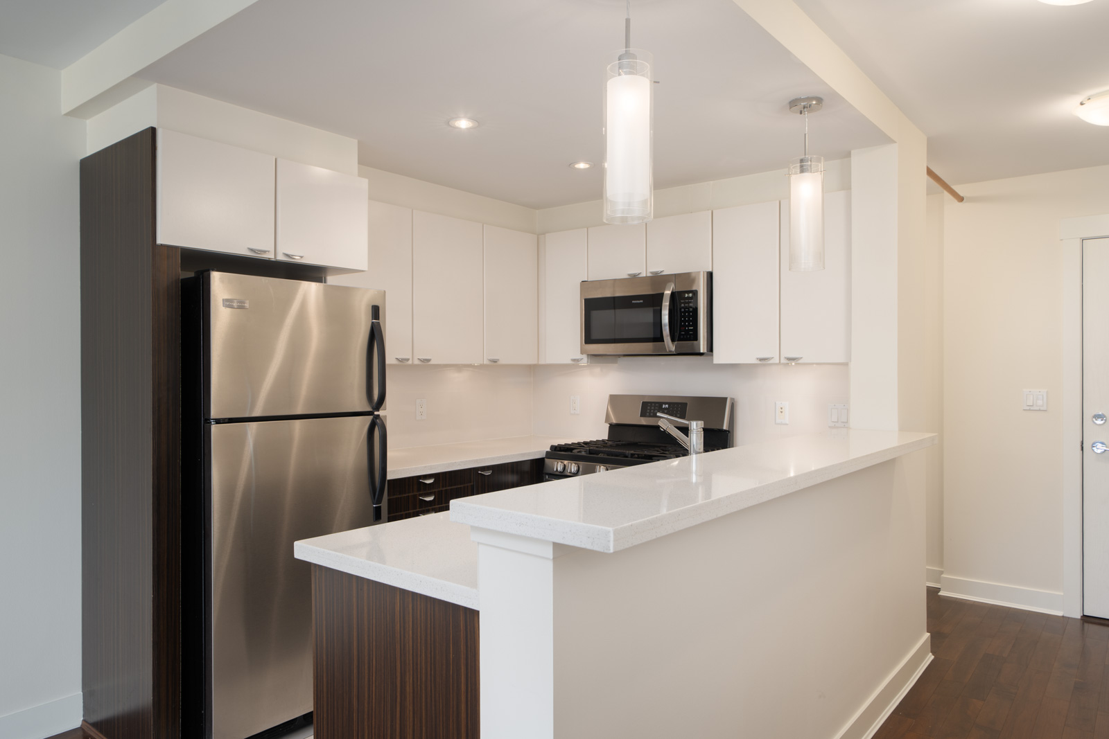Contemporary 5th-floor kitchen with white cabinets, stainless appliances, quartz counters, and dark wood floors in North Vancouver.