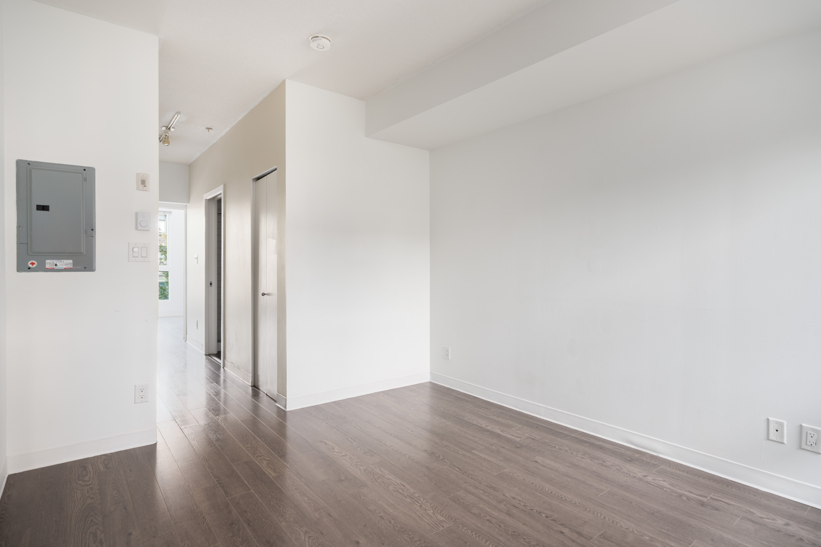 Empty room with white walls, dark wood floor, hallway with two doors, and electrical panel on the left at 138 E Hastings St, Vancouver.