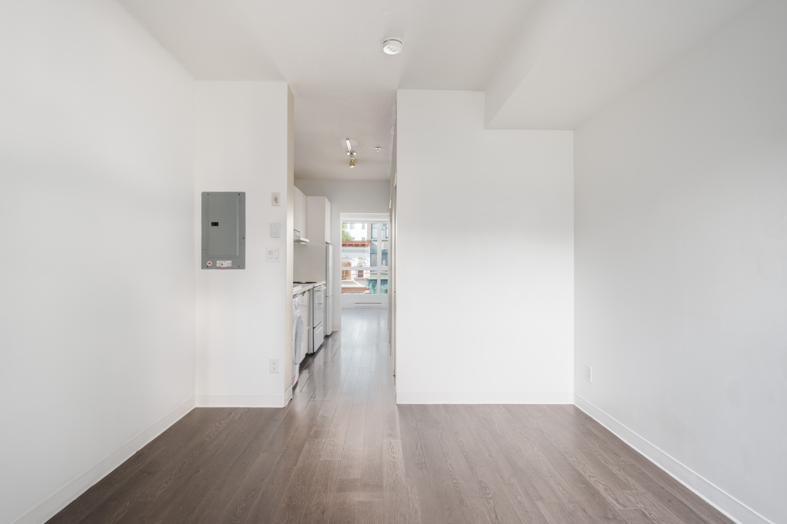 Unfurnished apartment with white walls, dark wood floors, kitchen appliances, and large window. 138 E Hastings St, Vancouver.