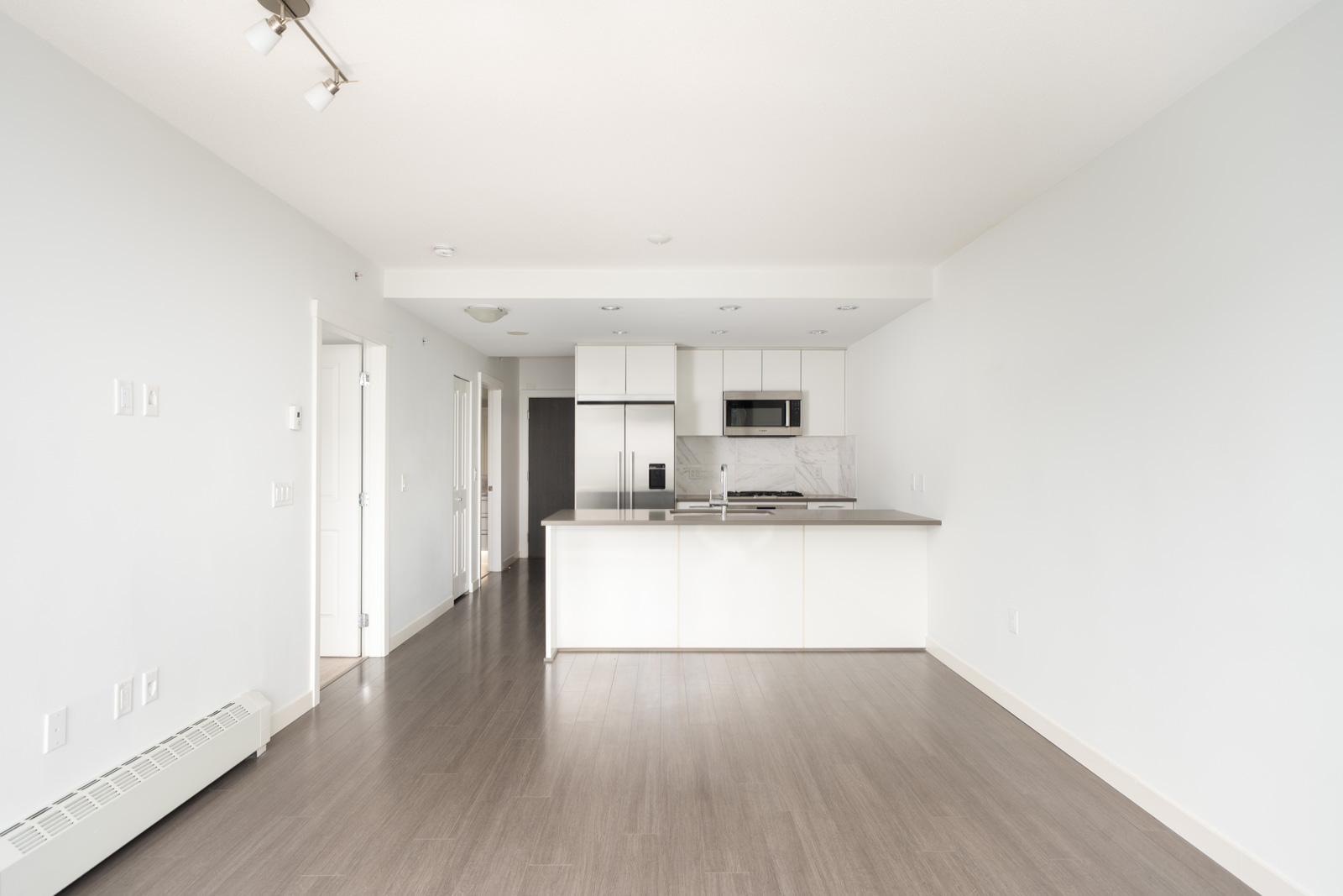 Empty modern kitchen in Vancouver apartment with white cabinets, stainless appliances, and light gray wood floors on 2nd floor.