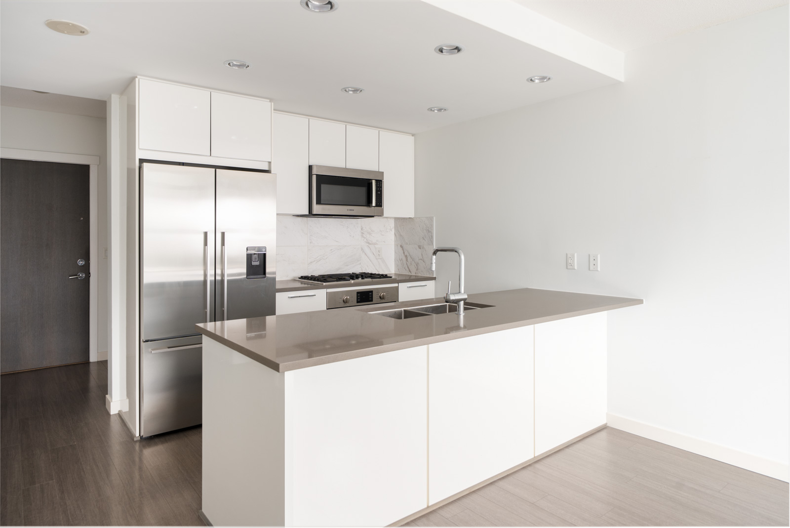 Modern kitchen on East Kent Ave, Vancouver with white cabinets, stainless appliances, marble backsplash, and island sink.