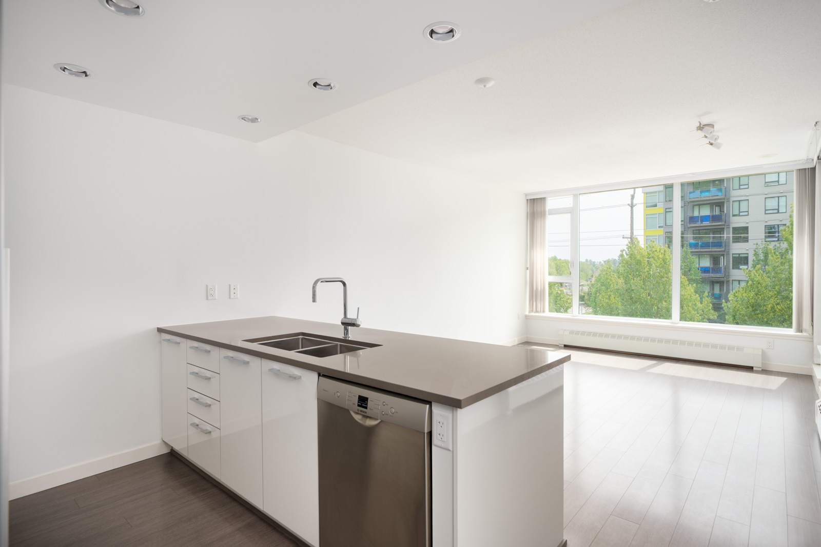 Unfurnished modern kitchen at 3281 East Kent Ave, Vancouver with white cabinets, stainless dishwasher, and large window with city view.