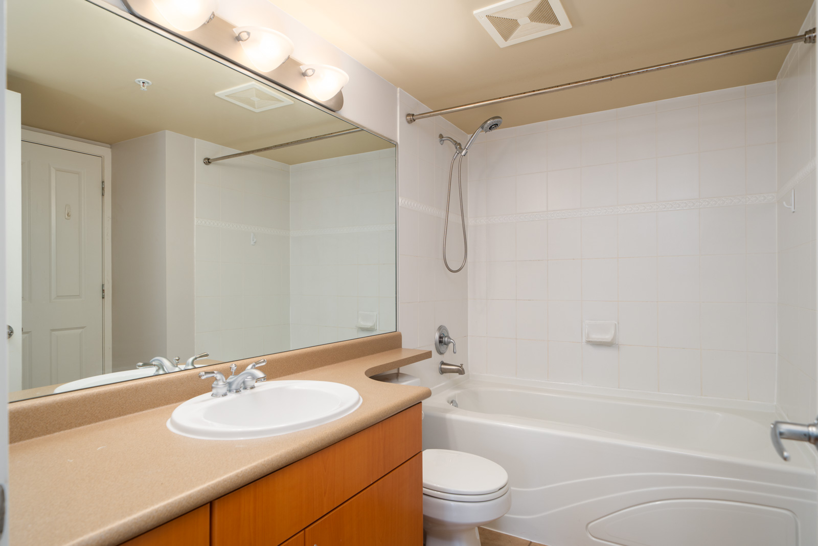 Modern bathroom in a Halifax St, Burnaby condo with large mirror, single sink vanity, toilet, and tub with white tile.