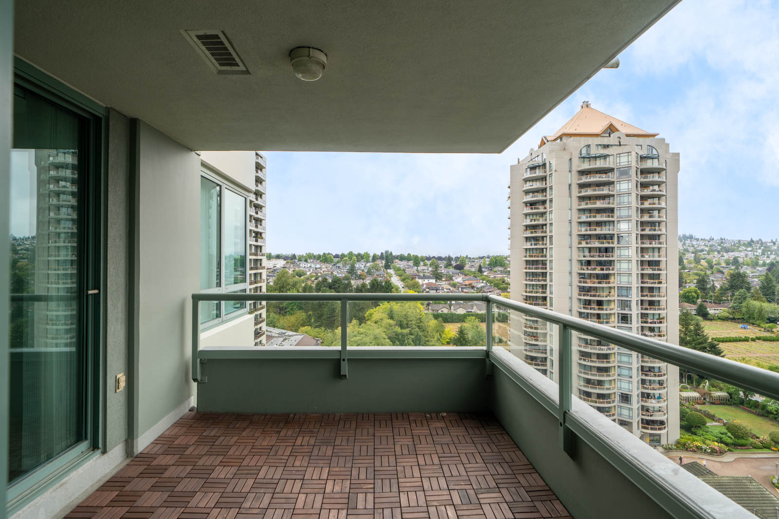 16th-floor Halifax St condo balcony with wood tile floor, glass railing, and views of nearby buildings, trees, and houses.