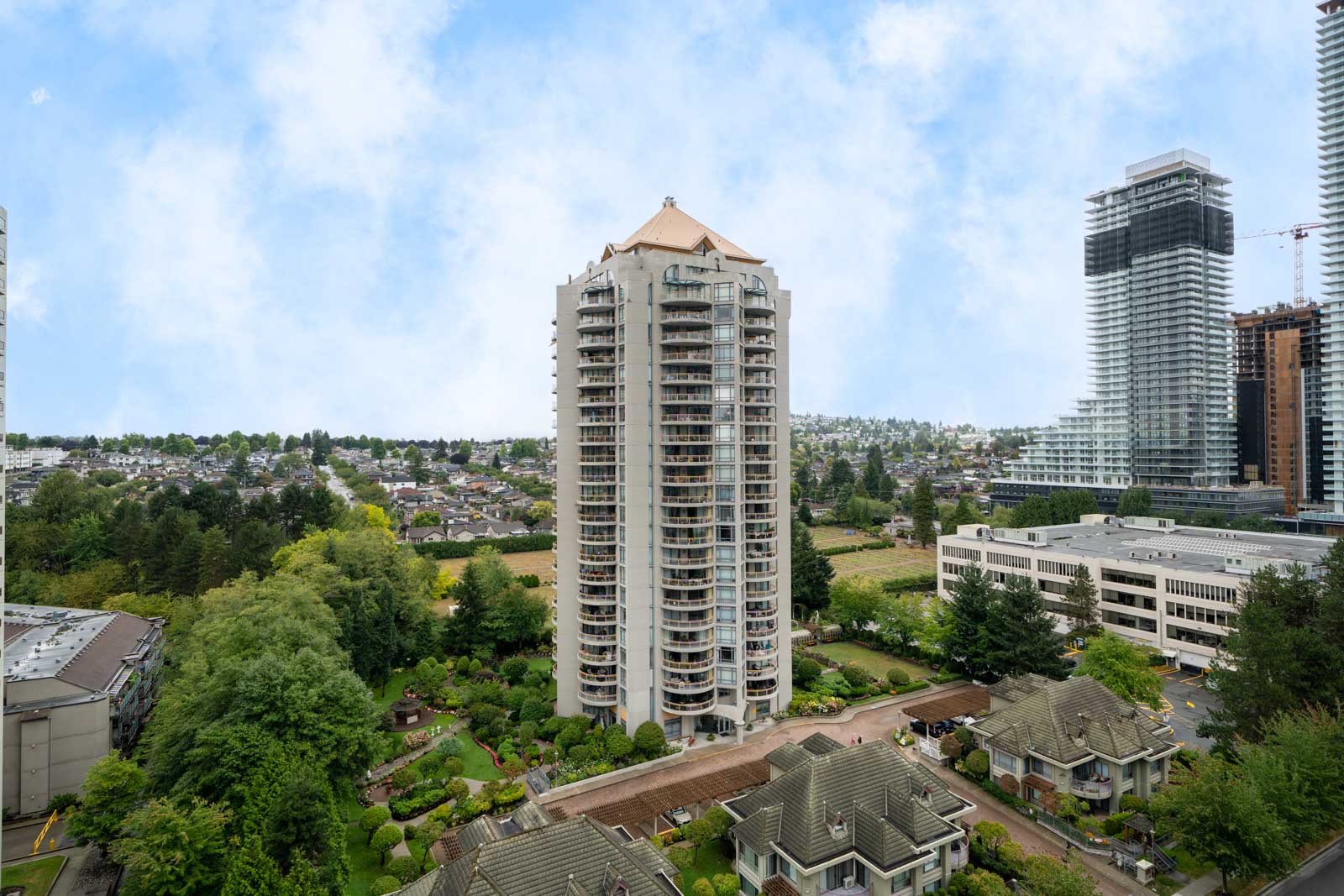 A tall residential building on Halifax St, Burnaby rises among trees and low-rises, with city high-rises in the background.