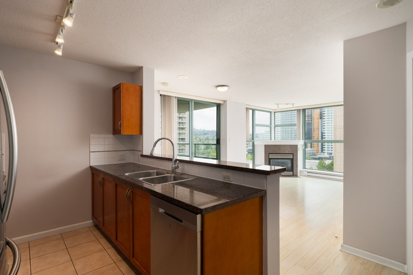Modern kitchen with wood cabinets, black countertops, open to bright living area with fireplace and city views in Burnaby.