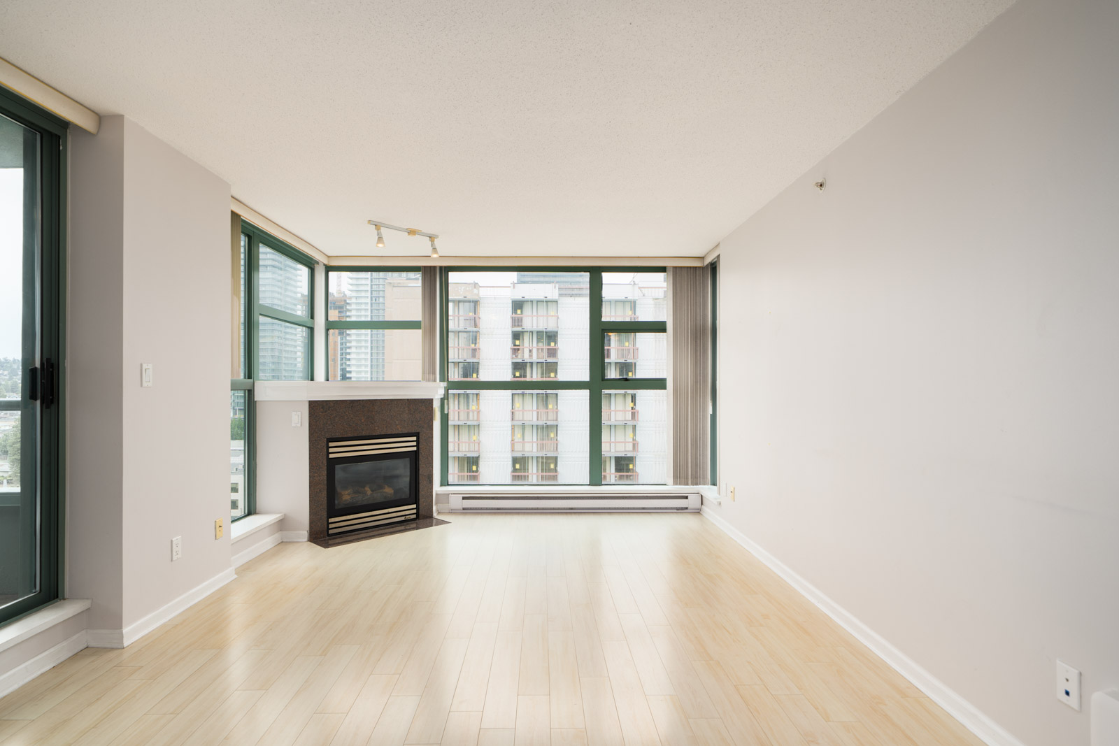 Unfurnished modern living room with light wood floors, large windows, fireplace, and city views in a 16th-floor Burnaby condo.