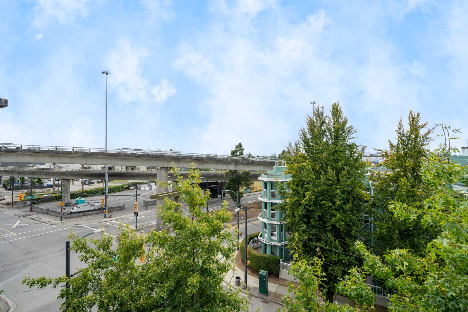 Urban intersection at 8988 Hudson St, Vancouver, featuring an overpass, traffic lights, trees, and a modern glass building.