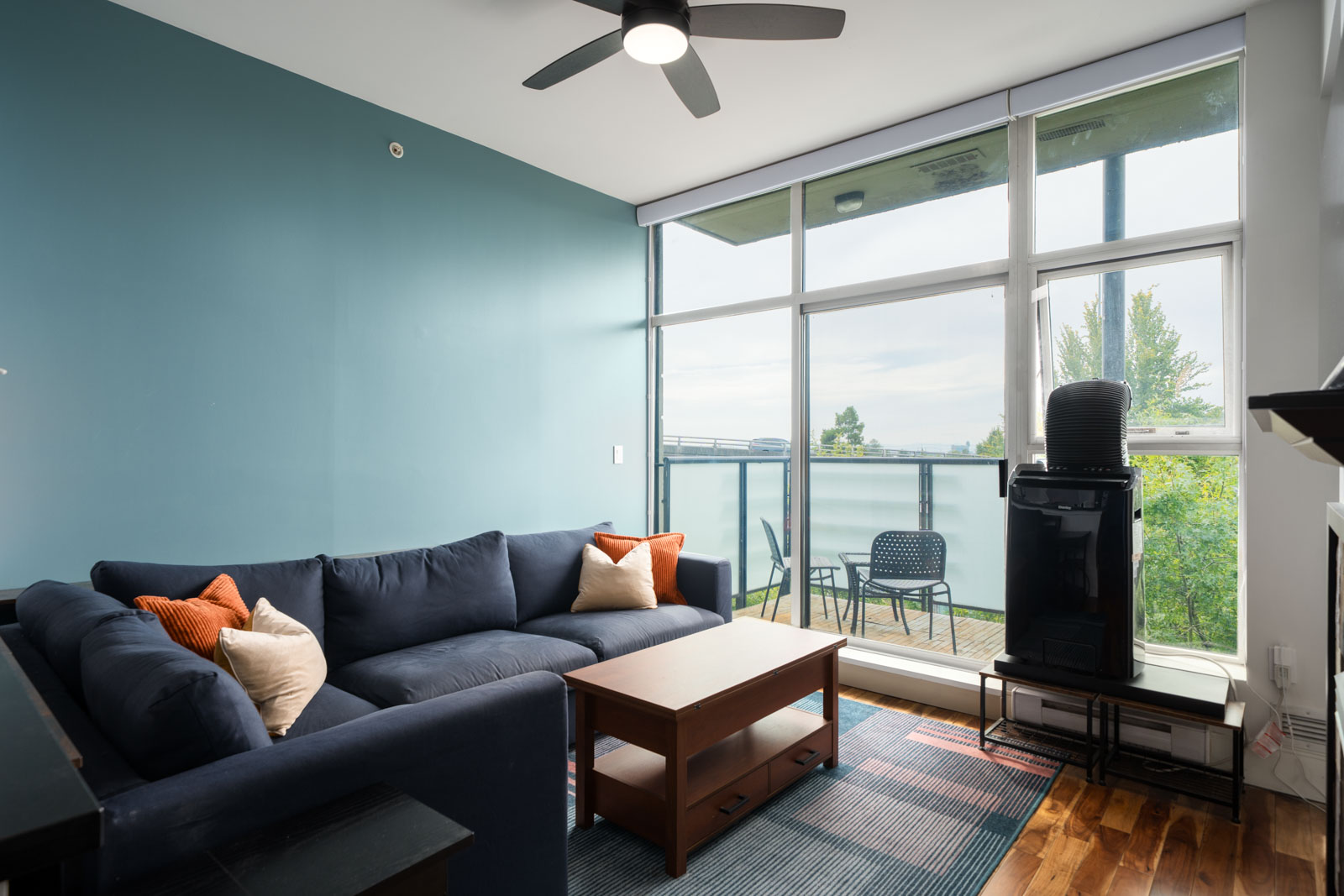 Modern living room on Hudson St, Vancouver with navy sectional, wood coffee table, blue accent wall, large windows, and balcony seating.