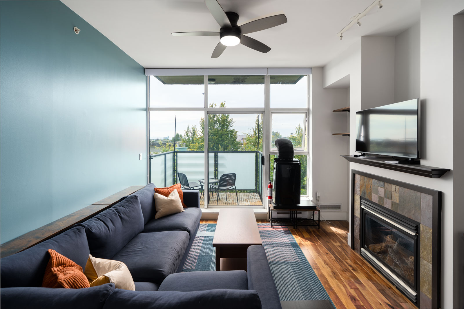 Modern living room on Hudson St, Vancouver, with blue walls, sectional sofa, fireplace TV, large windows, and balcony seating.