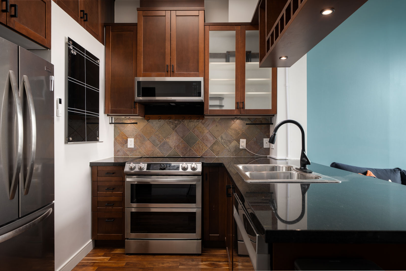 Modern Vancouver kitchen on Hudson St with stainless appliances, dark wood cabinets, black counters, double sink, tiled backsplash.