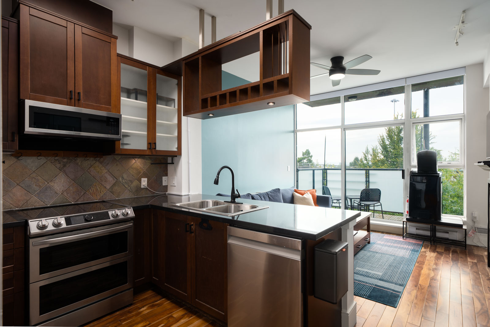 Modern kitchen with dark wood cabinets, stainless appliances, and black countertop, open to bright living area in Vancouver.